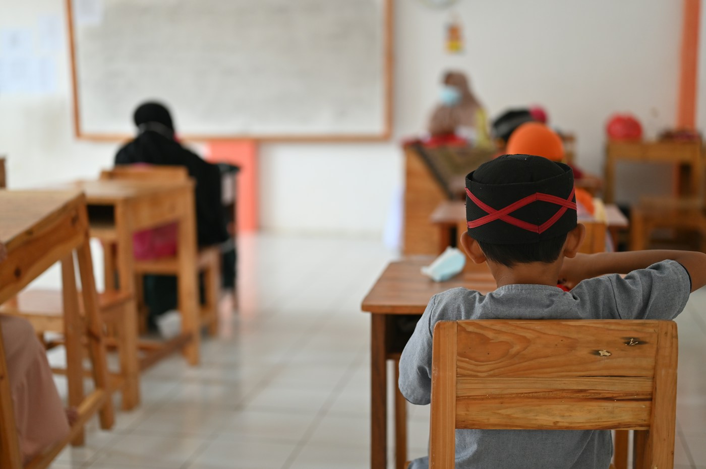 Élèves vus de dos, assis à leurs tables dans une classe.