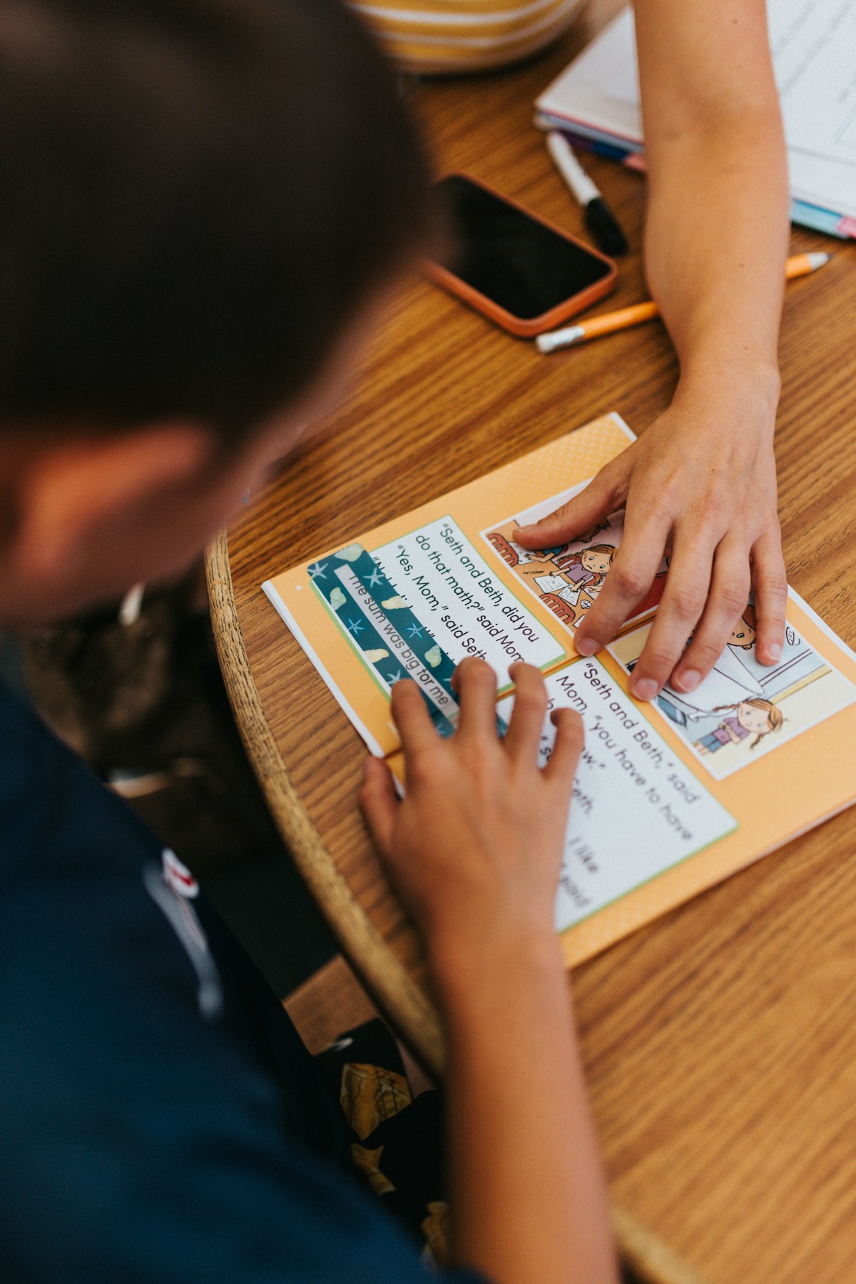 Enfant vu du dessus travaillant sur une fiche de lecture, sans visage visible.